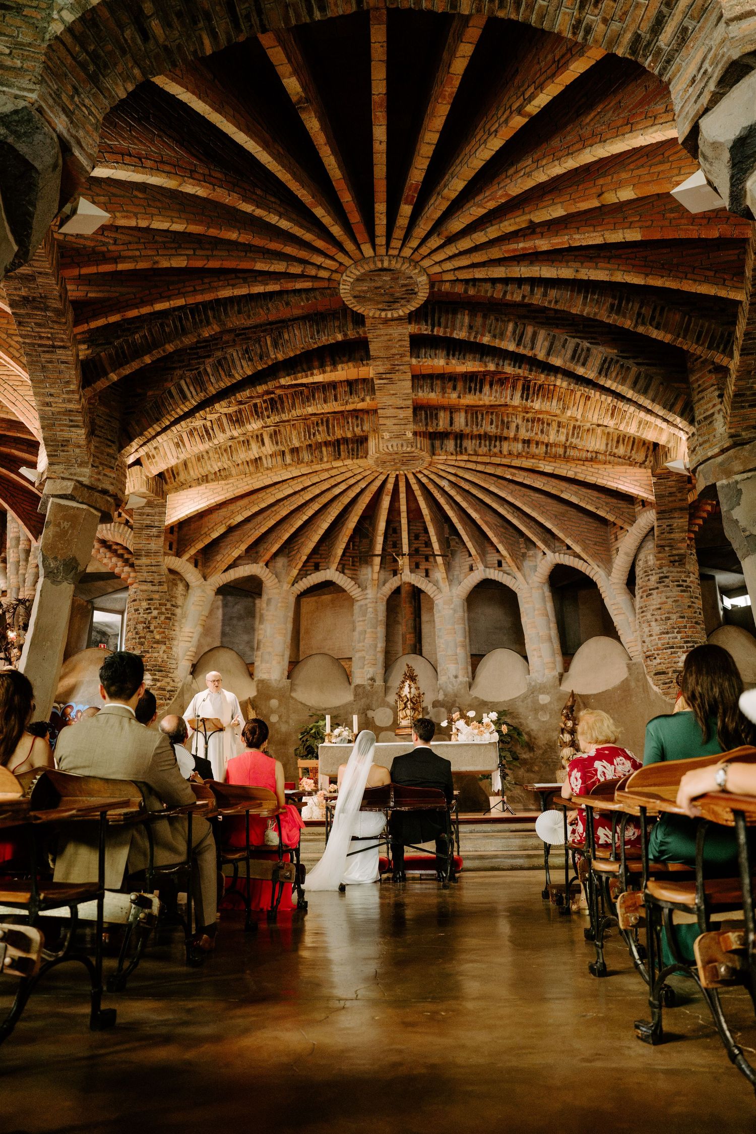 Wedding ceremony inside Gaudi's Crypt at Colonia Guell, featuring stunning brick vaulted ceiling and arches.