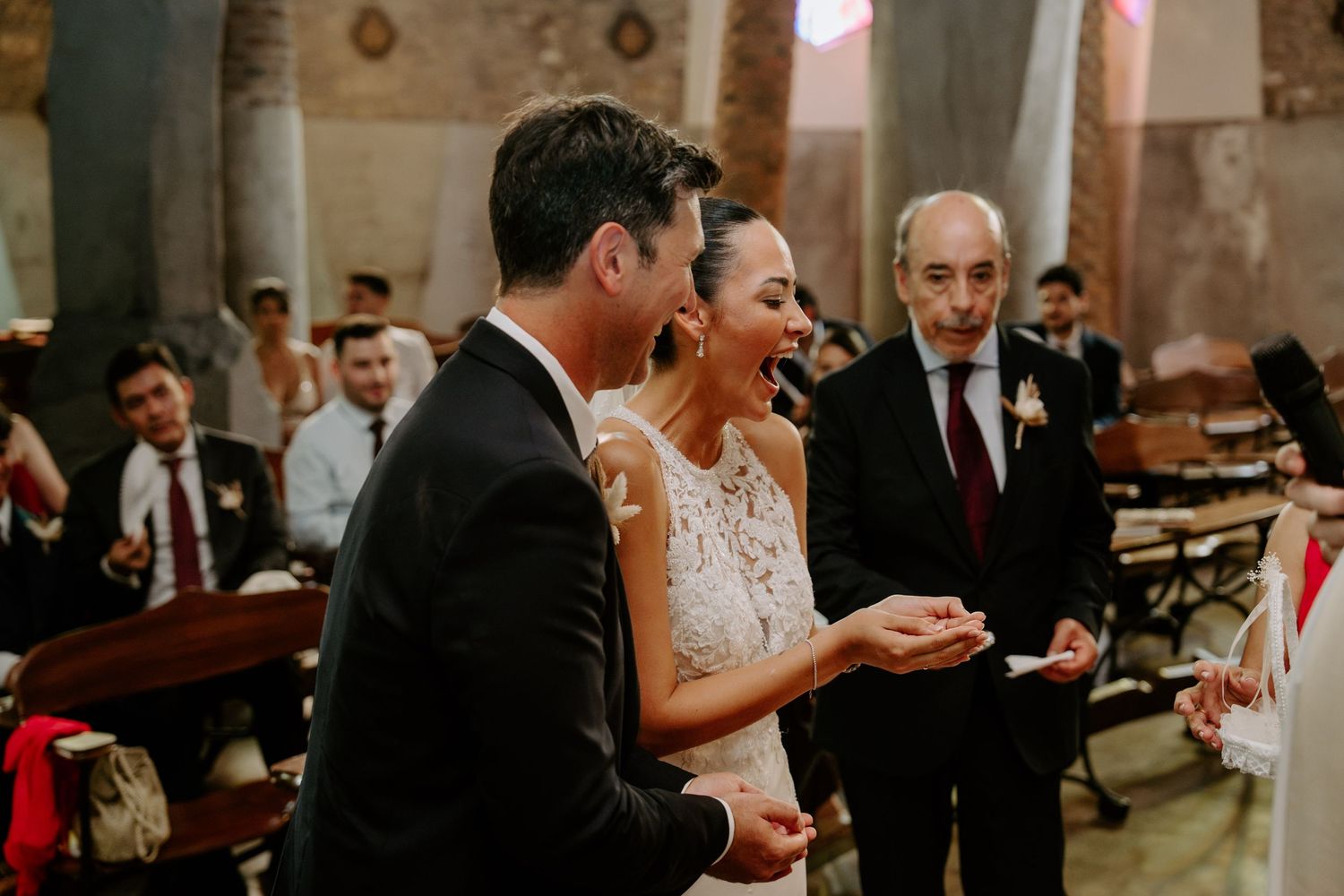Bride and groom exchanging rings during wedding ceremony in a rustic church with guests applauding.