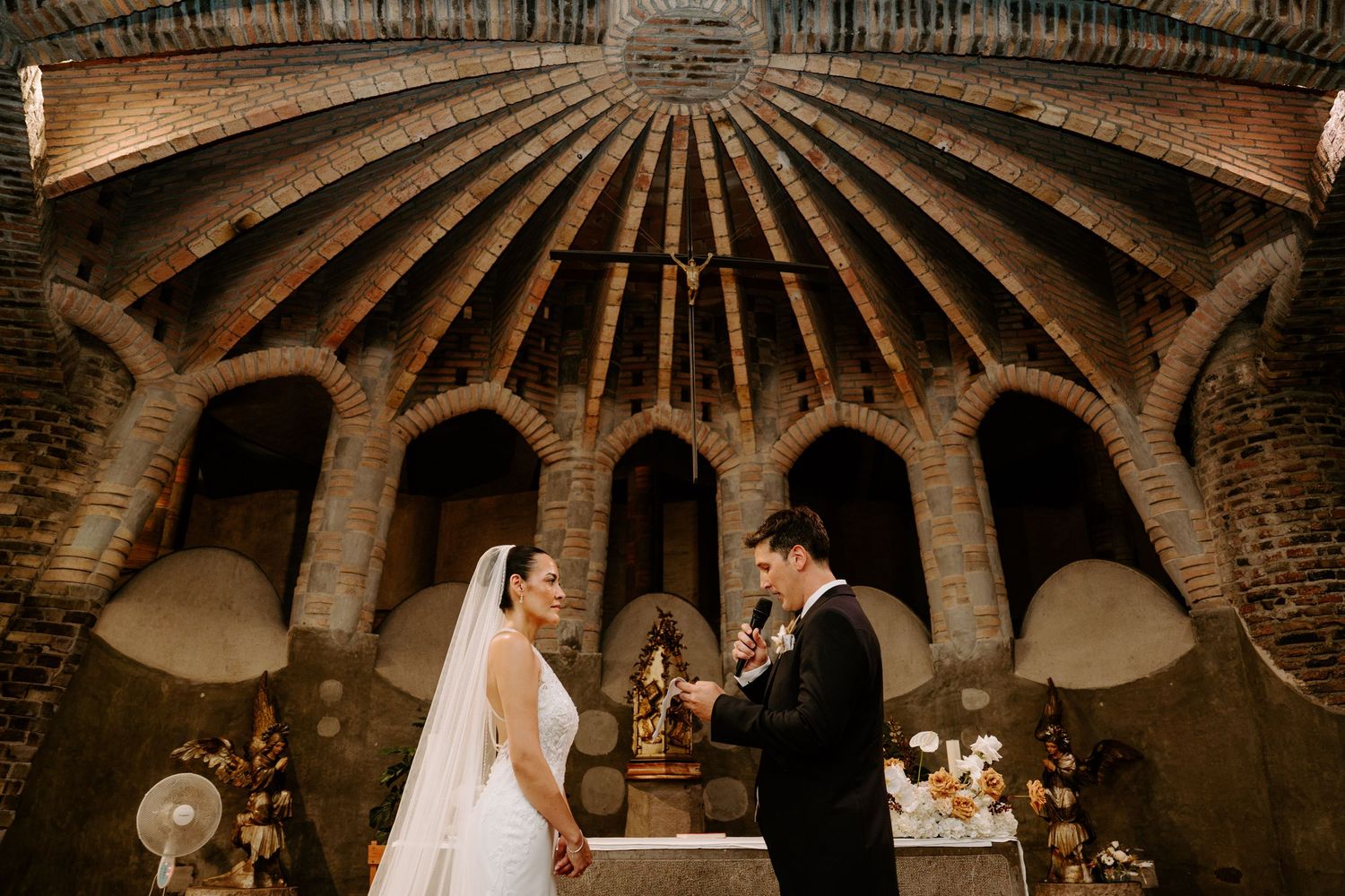 Bride and groom exchange vows beneath stunning brick domed ceiling in historic wedding venue.