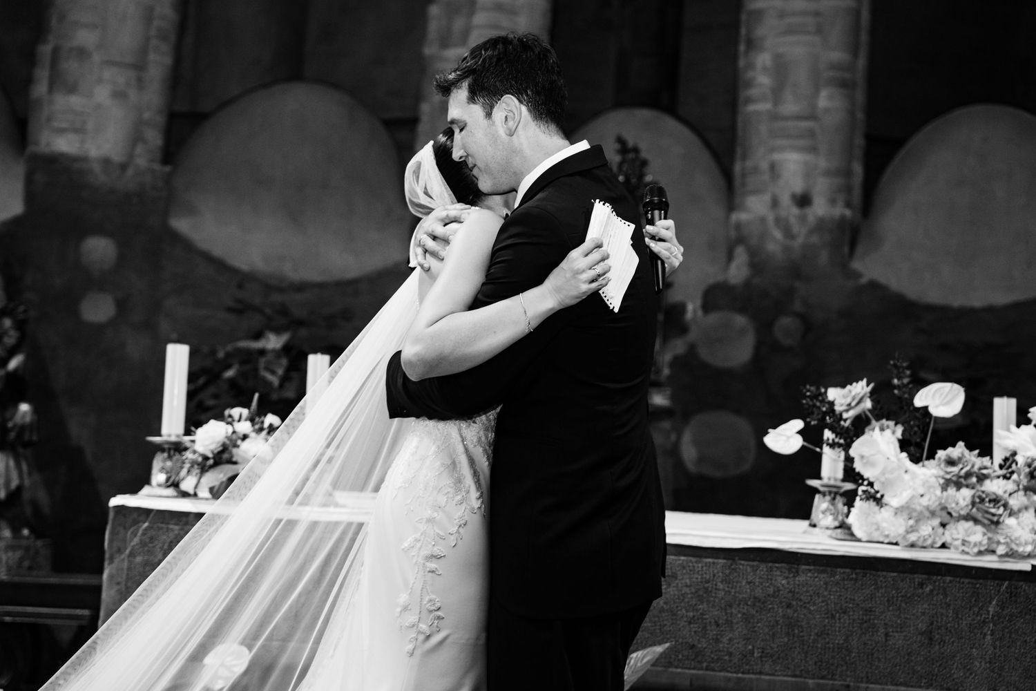 Black and white photo of bride and groom sharing first embrace at altar after wedding ceremony.