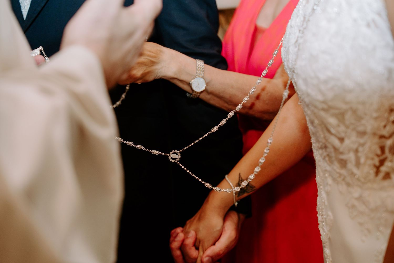 Close-up of hands joined with rosary during traditional wedding ceremony blessing ritual.