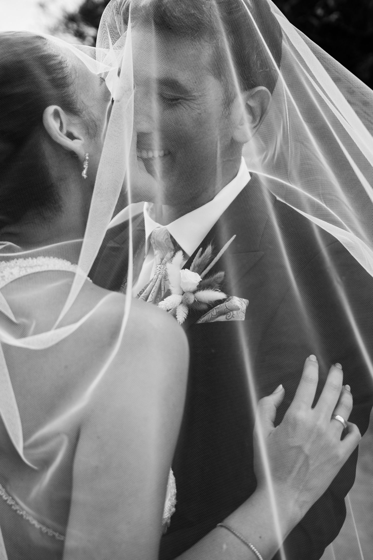 Black and white romantic photo of bride and groom kissing under flowing wedding veil.