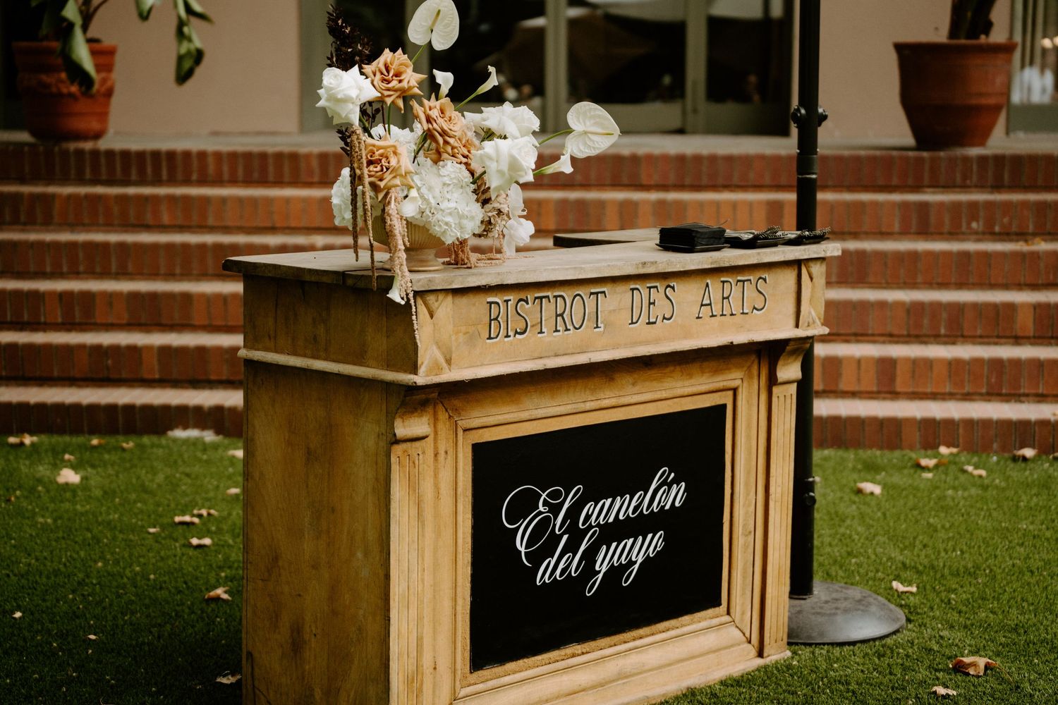 Rustic wooden bar station with floral arrangement and chalkboard sign reading El canonlon del yayo.
