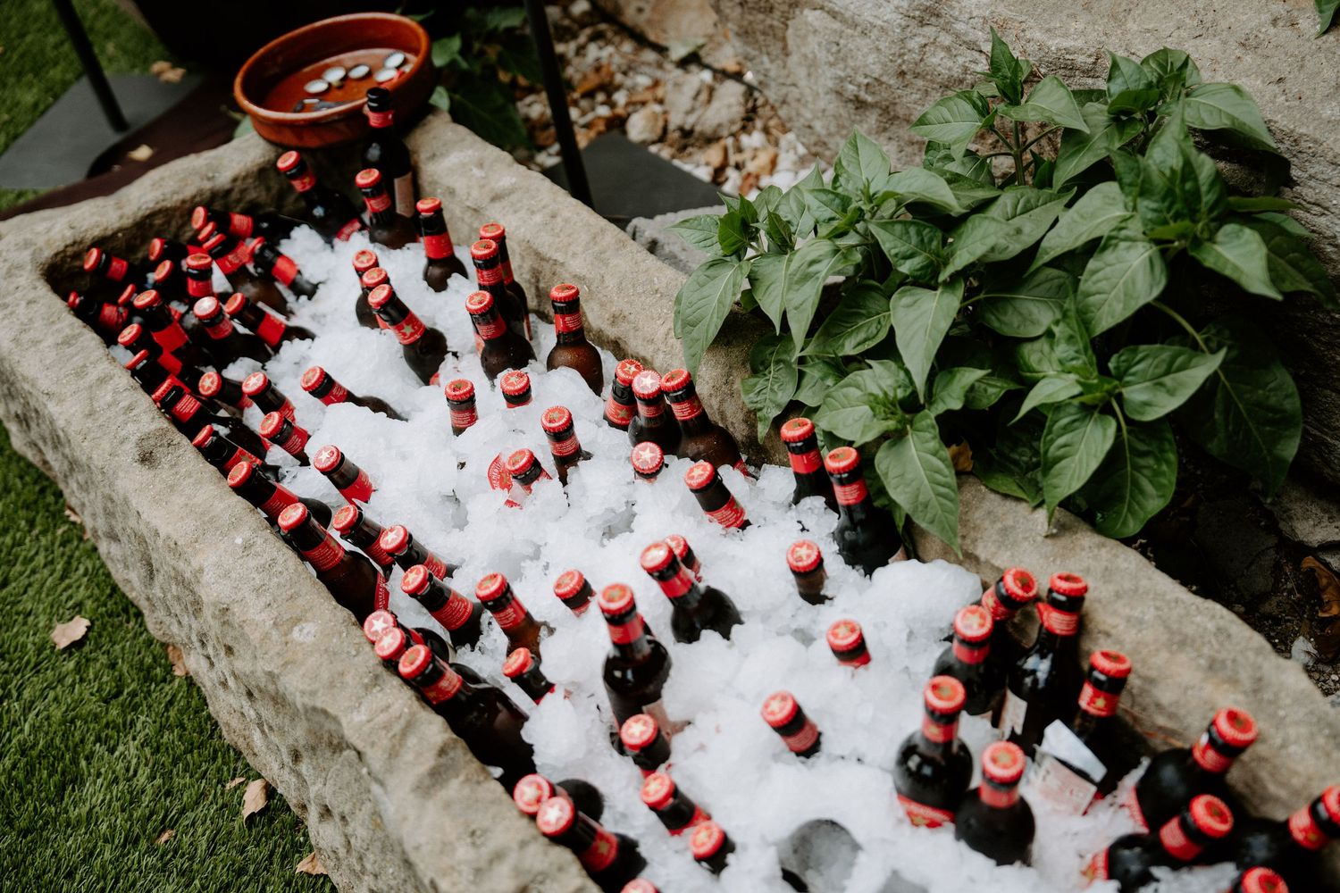 Cold Coca-Cola bottles packed in ice in stone trough for outdoor wedding reception drinks.
