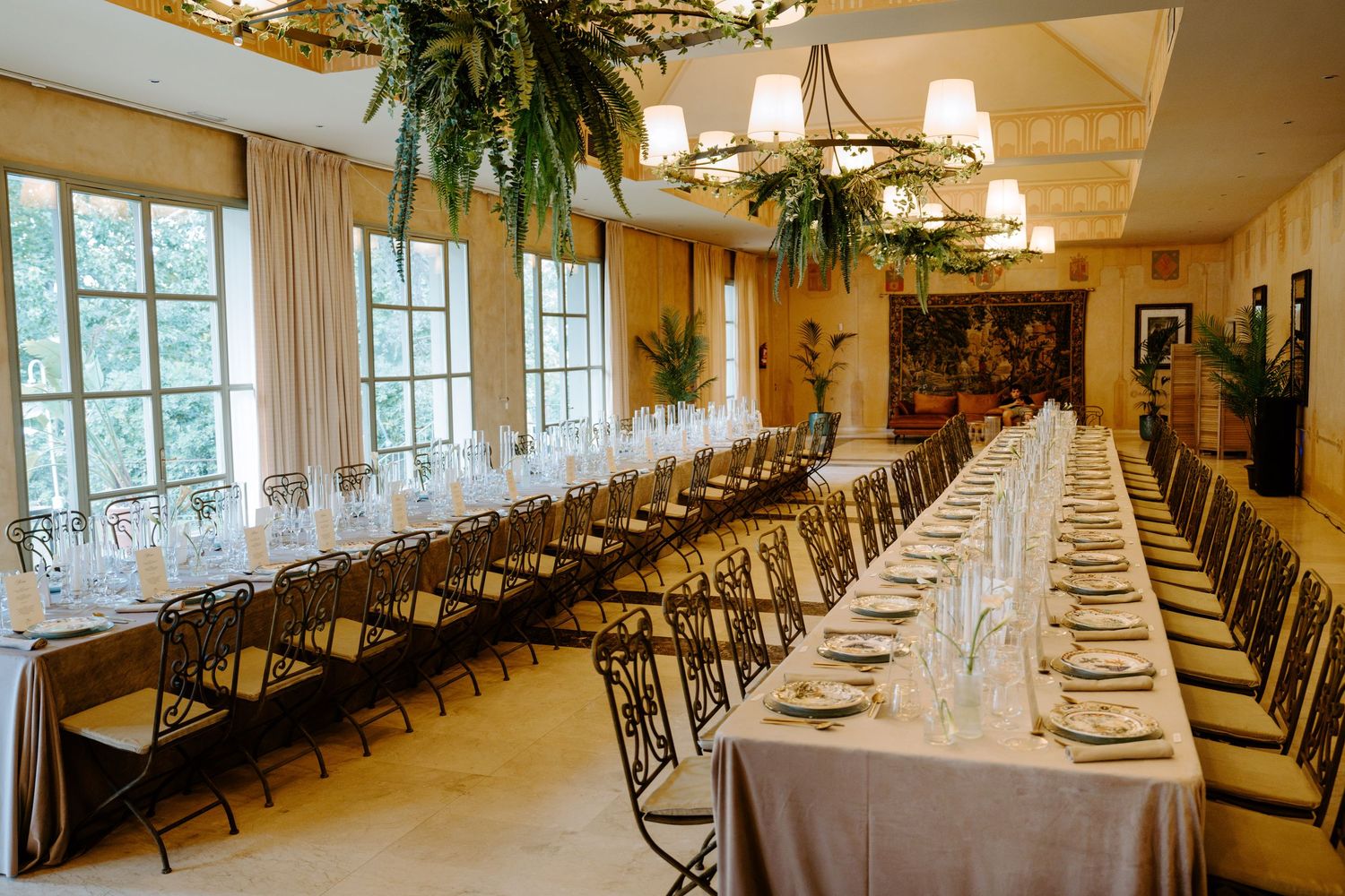 Elegant wedding reception hall with long tables set for dining, adorned with lush green floral chandeliers.