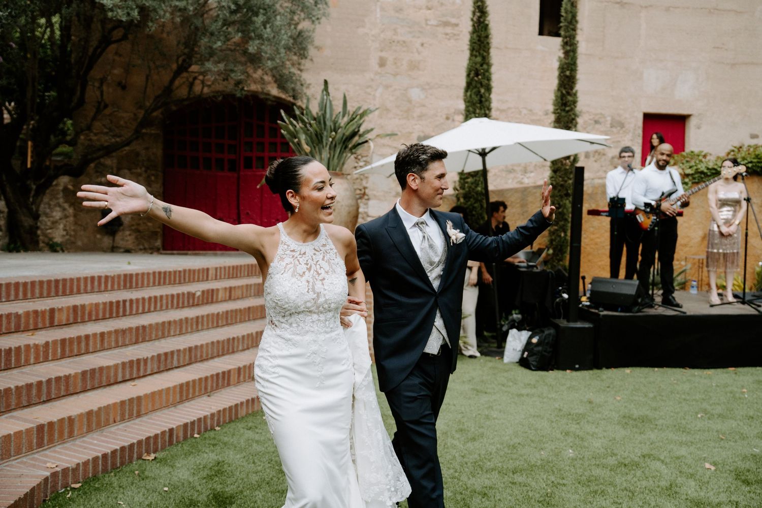 Excited bride and groom make grand entrance at outdoor wedding reception with live band.