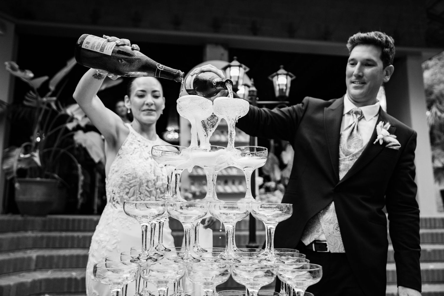 Bride and groom pouring champagne tower at elegant black and white wedding reception.