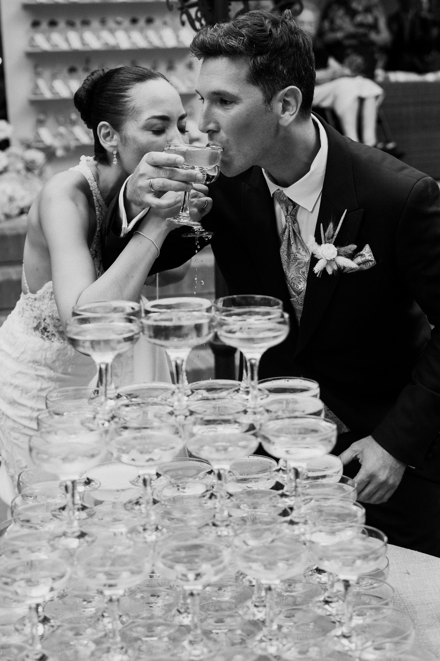 Newlyweds sip champagne together from a coupe tower in this romantic black and white wedding reception photo.