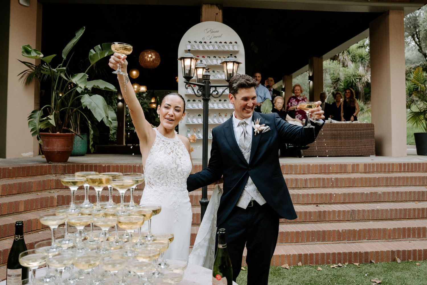 Bride and groom celebrate with champagne tower at outdoor wedding reception venue.