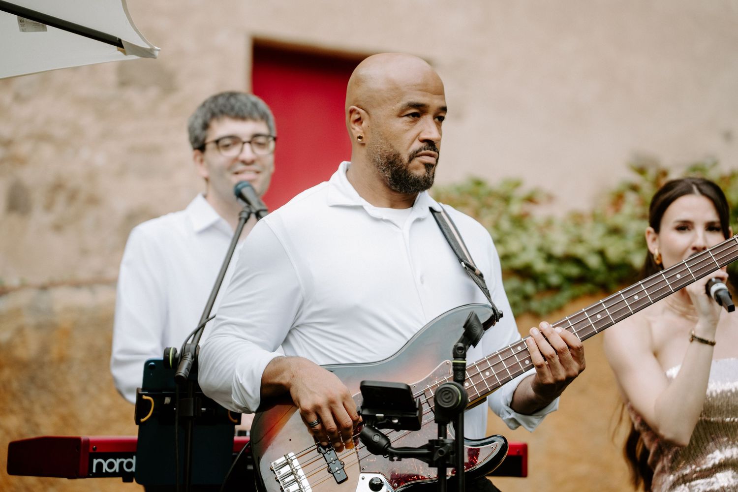 Live band performing outdoors with guitarist in white shirt and female vocalist at wedding reception.