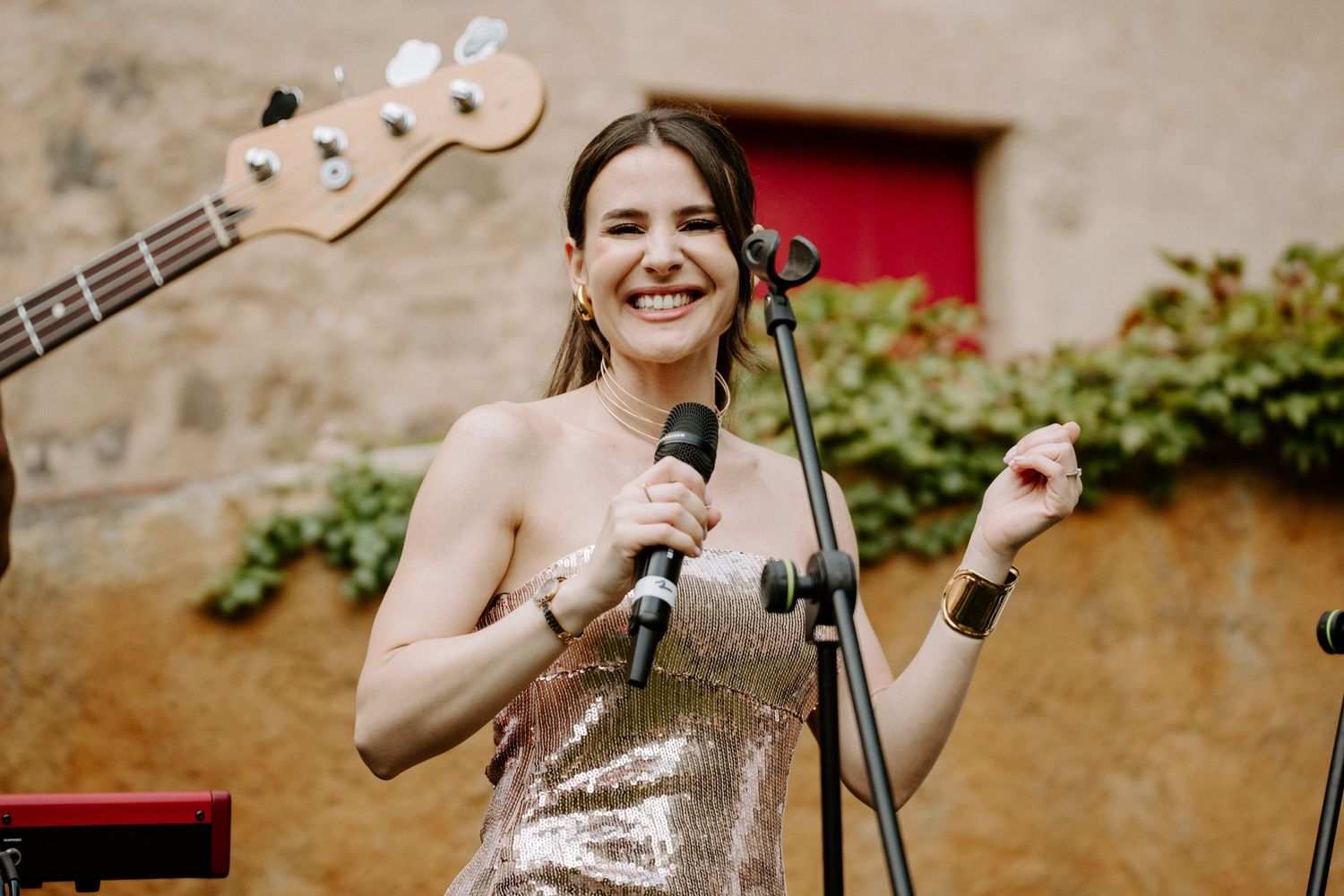 Smiling female singer in sequin dress performing at outdoor wedding reception with microphone and band.