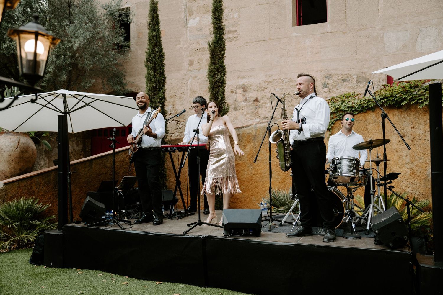 Live wedding band performing outdoors with female vocalist at elegant garden venue.