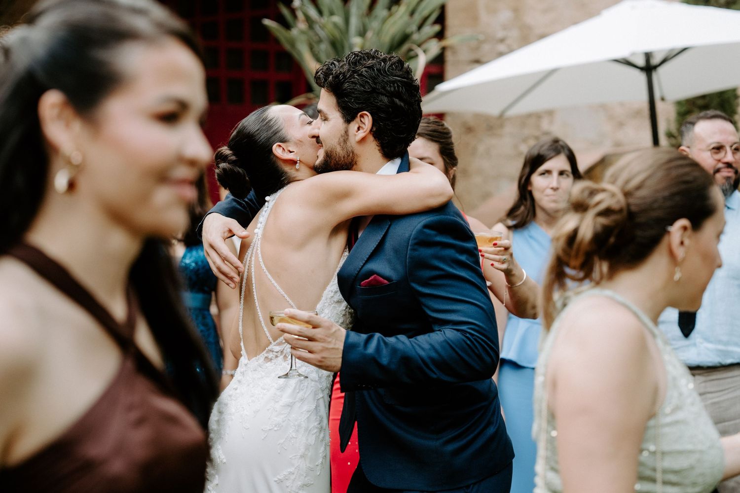 Bride and groom sharing romantic kiss while guests celebrate at outdoor wedding reception.