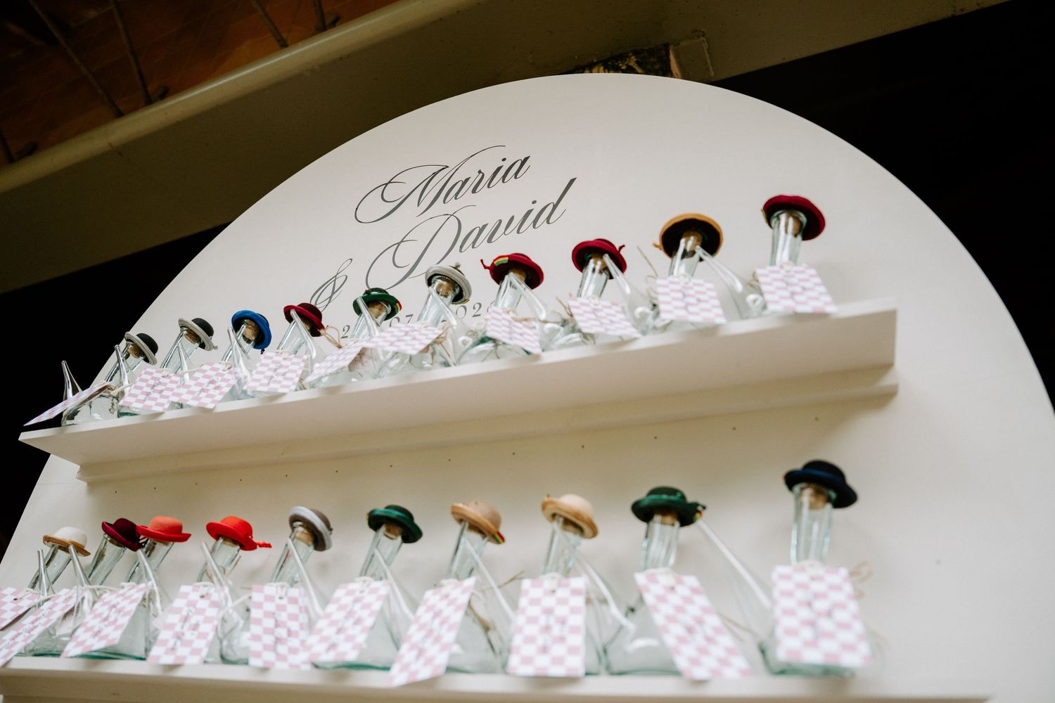 Wedding favor display featuring Maria and David name sign with decorative bottled gifts on shelves.
