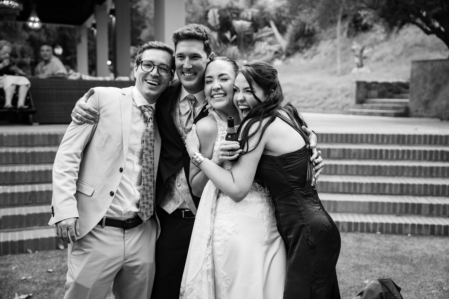 Black and white photo of bride and groom posing with two friends at an outdoor wedding reception.
