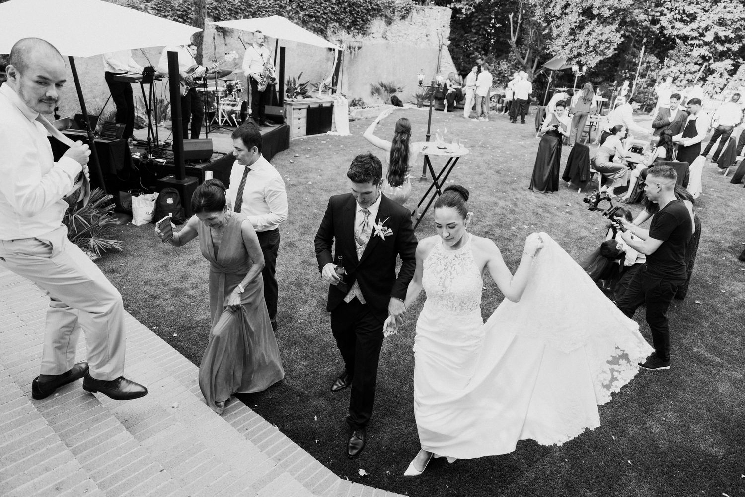 Black and white photo of bride and groom making grand entrance at outdoor wedding reception with guests cheering.