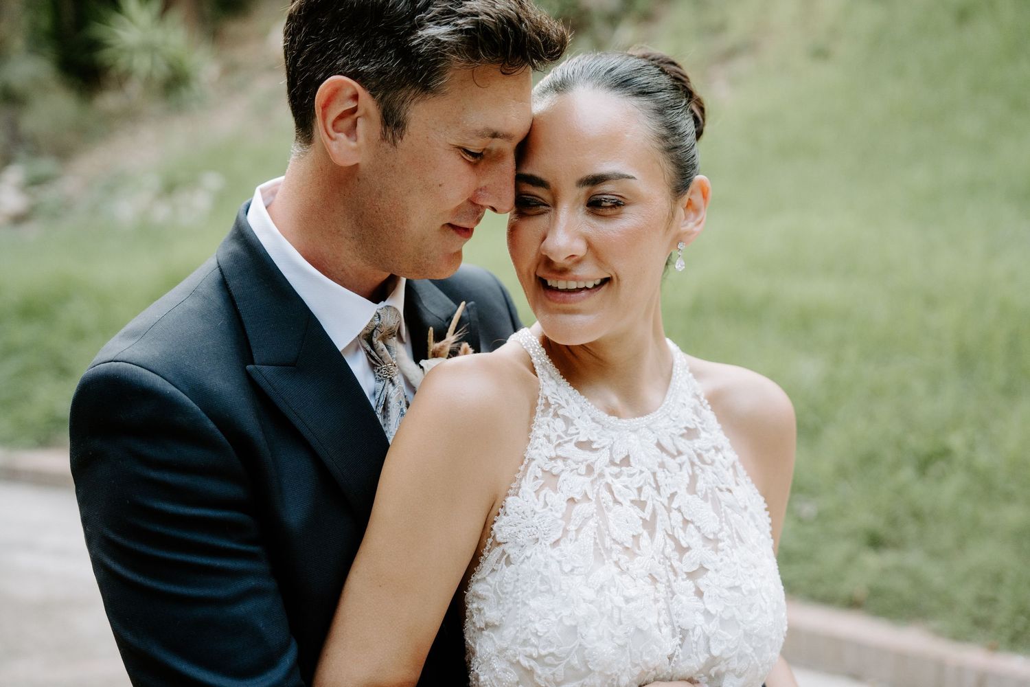 Bride and groom share an intimate moment, with the groom embracing the smiling bride in a lace halter wedding gown.