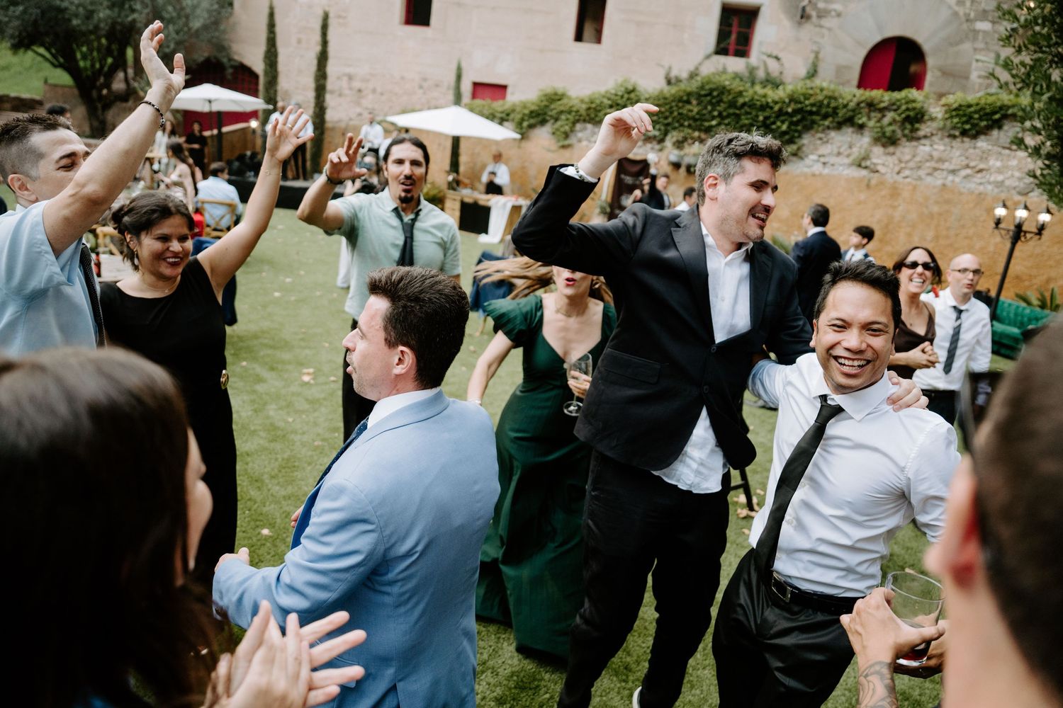 Wedding guests celebrating and dancing joyfully on a lawn at an outdoor reception.