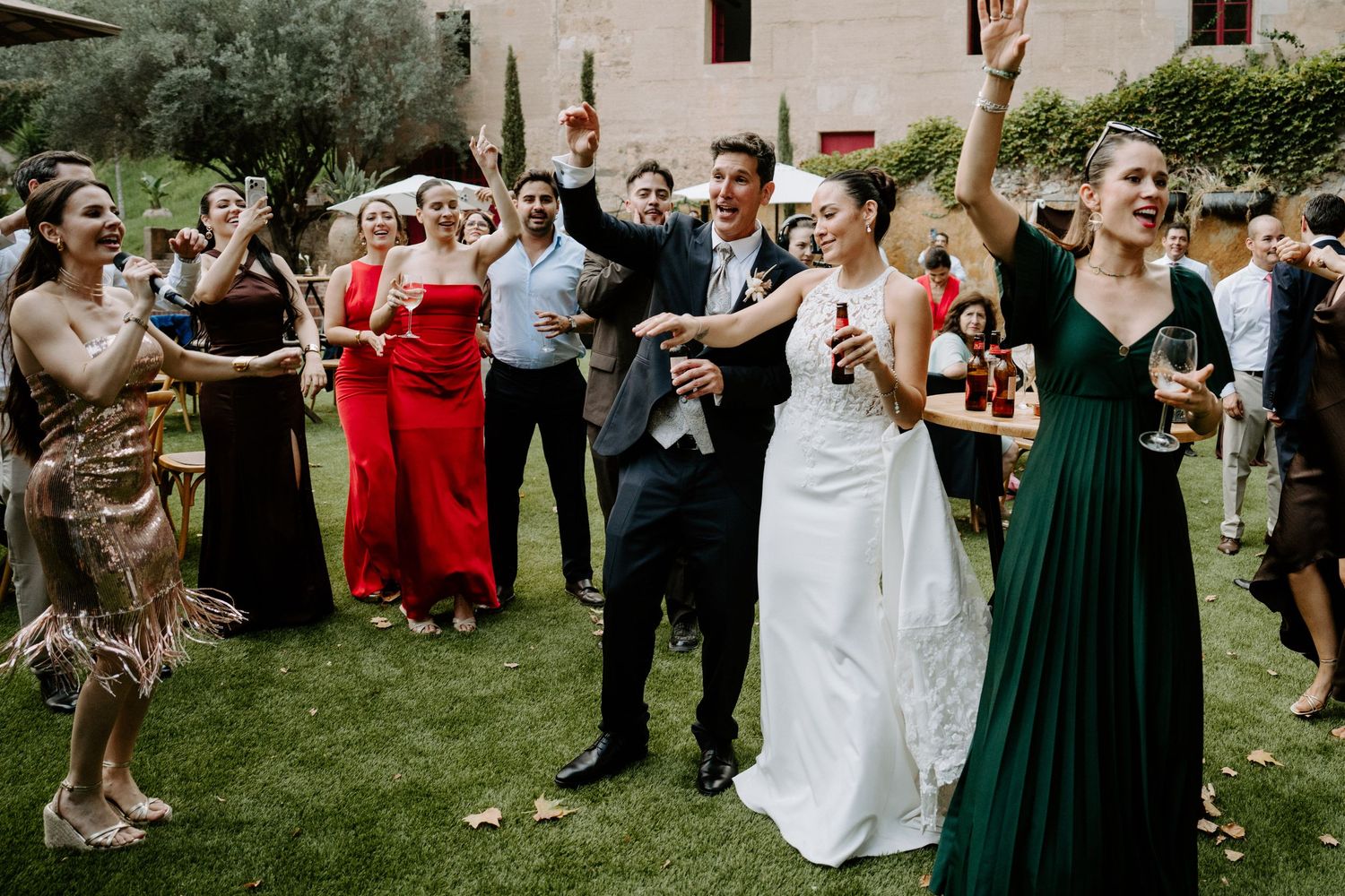 Wedding couple celebrating outdoors with guests in formal attire raising glasses.