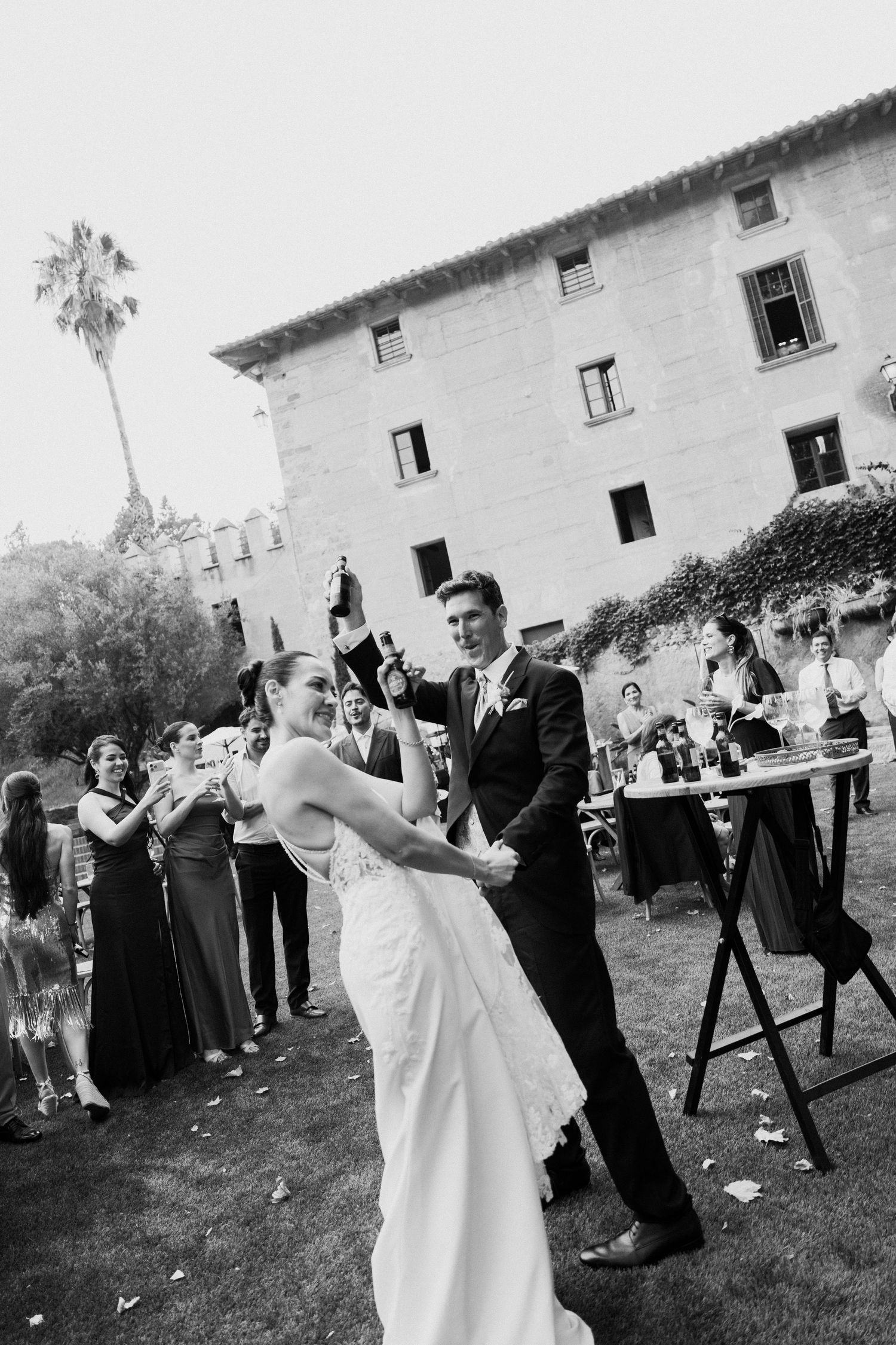 Bride and groom share first dance outdoors with wedding guests cheering in background.