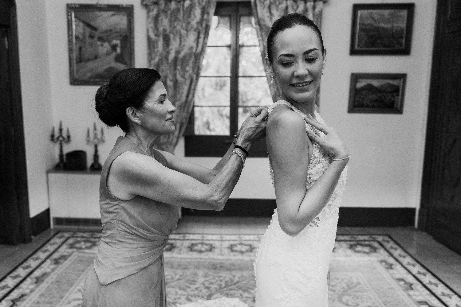 Mother helps bride with wedding dress buttons in a classic black and white getting ready photo.
