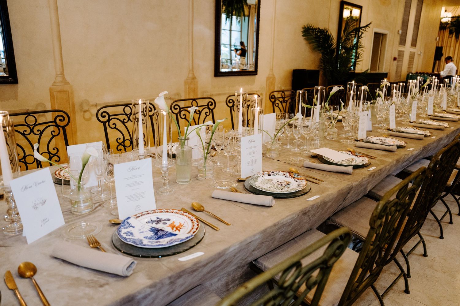 Elegant long wedding reception table set with fine china, gold cutlery, and glassware.
