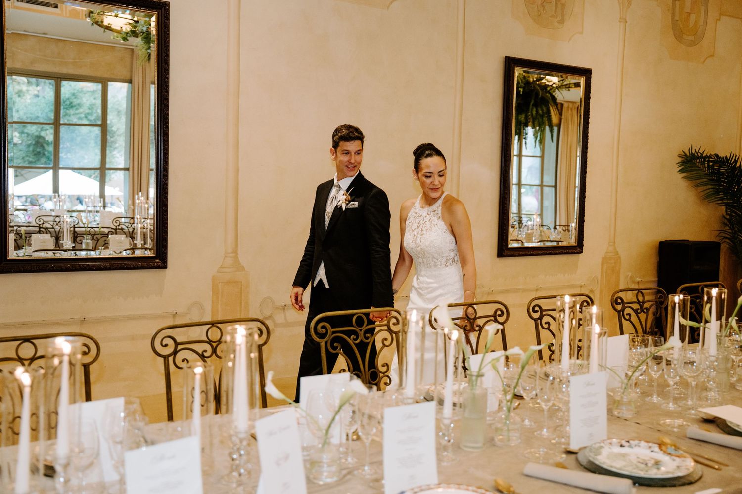 Elegant wedding couple standing in a beautifully decorated reception hall with long dining tables set for guests.