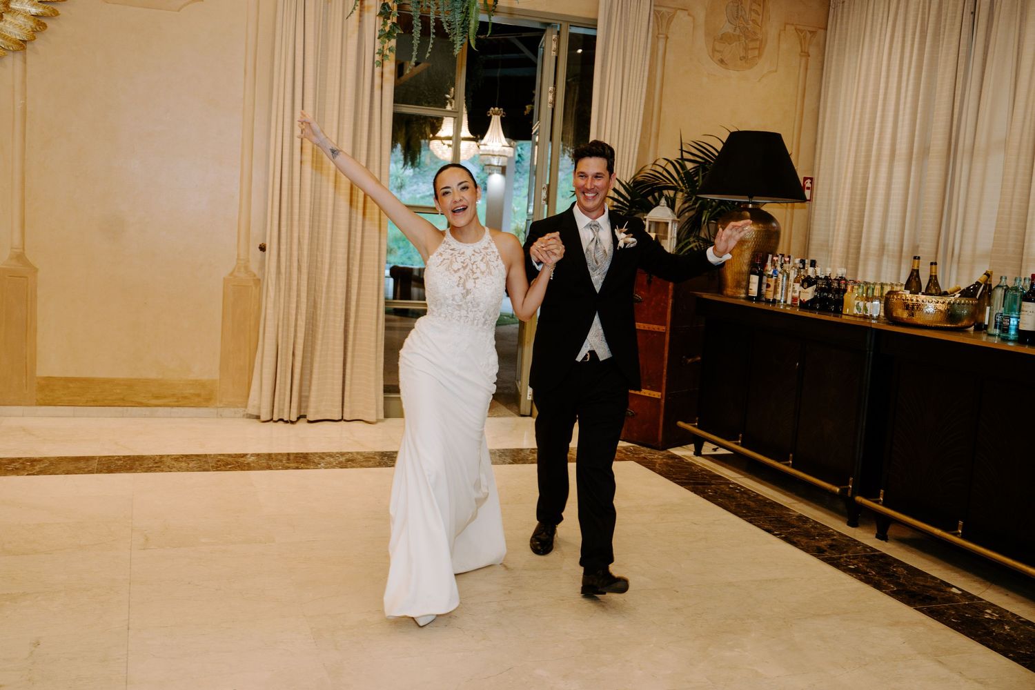 Joyful newlyweds make grand entrance at wedding reception, bride in white gown and groom in black tuxedo.