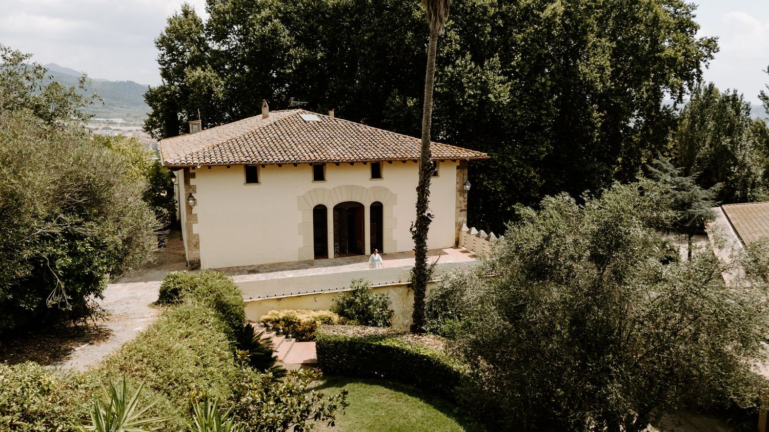 Charming rustic villa surrounded by lush trees and manicured gardens on a sunny day.