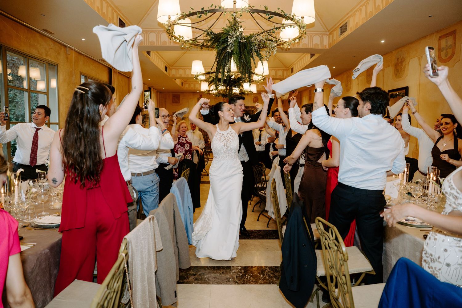Bride entering wedding reception hall as guests wave white napkins in celebration.