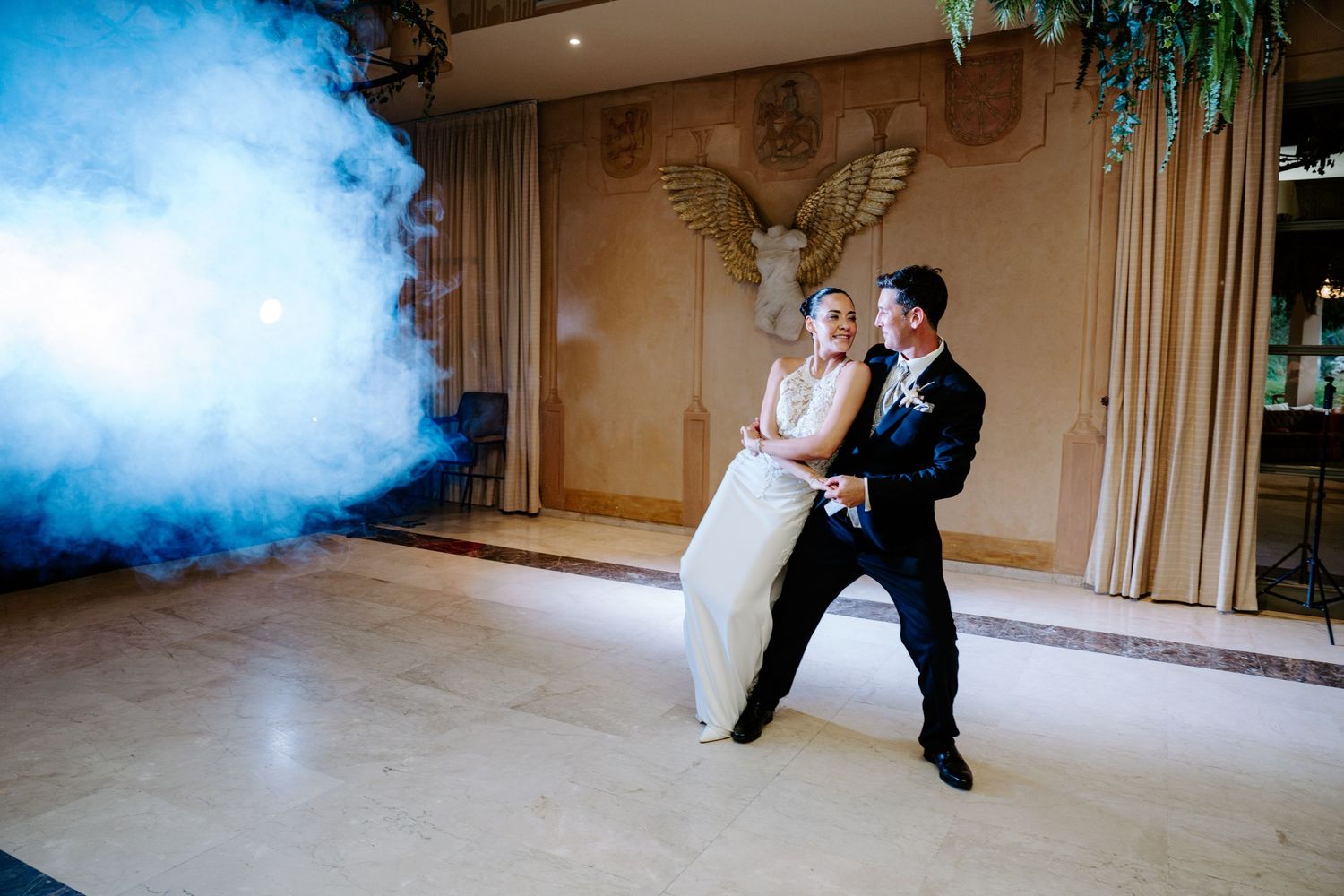 Bride and groom share first dance surrounded by dramatic blue smoke on a dance floor in an elegant ballroom.