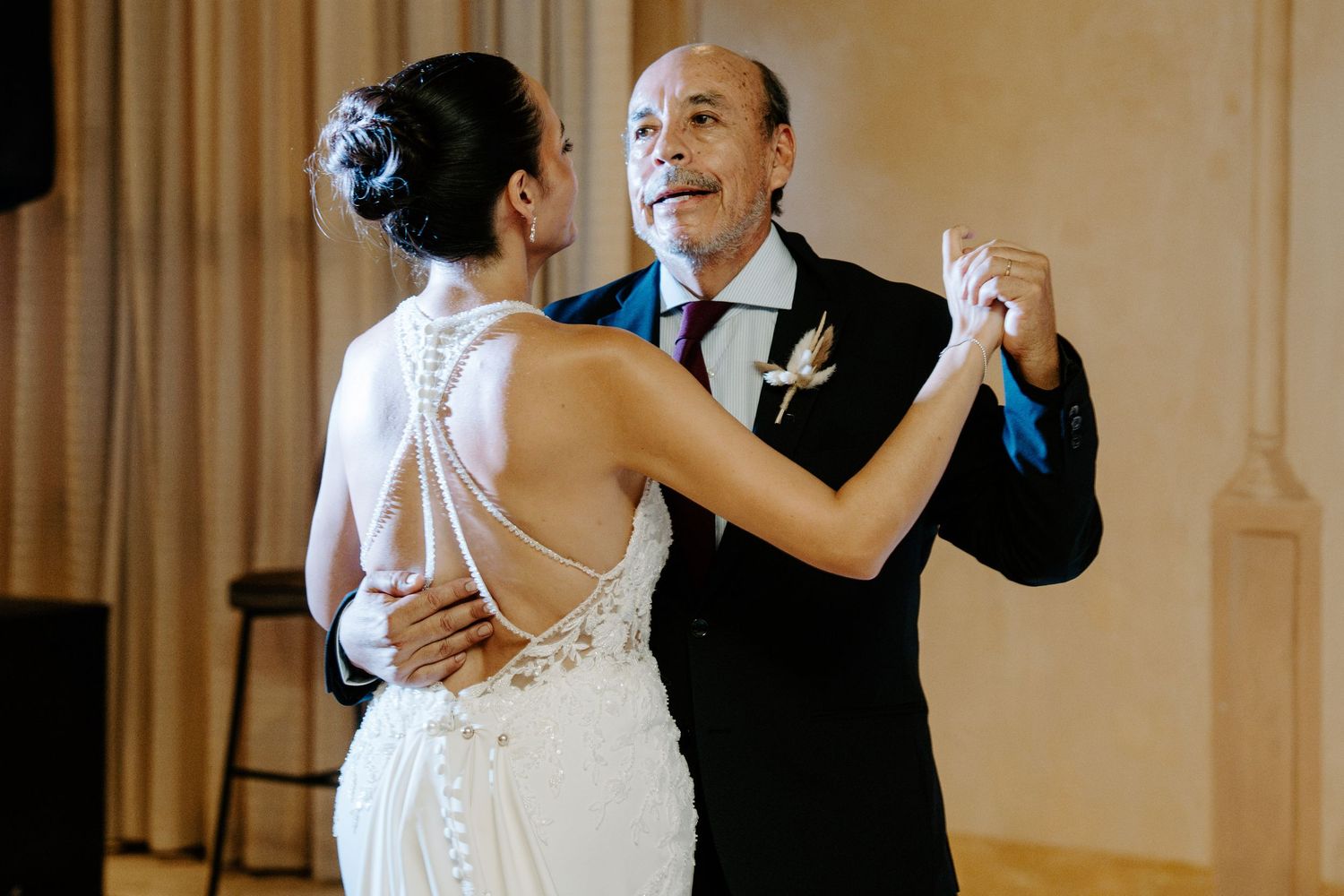 Bride in backless beaded gown shares a tender father-daughter dance at her wedding reception.