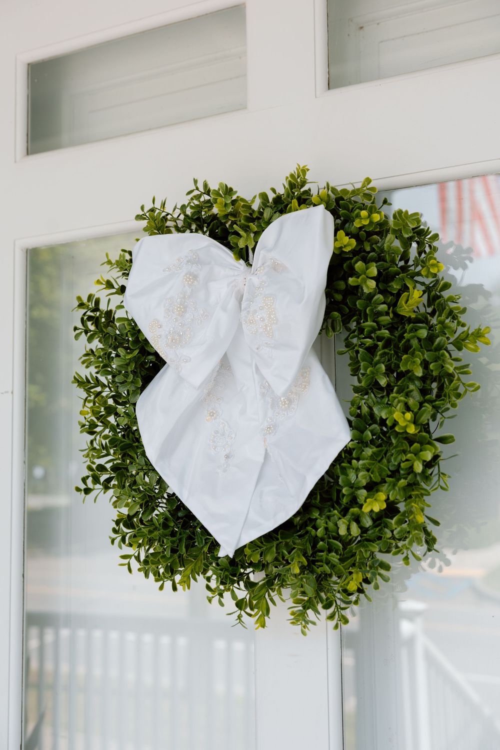 Green boxwood wreath with white bow on white door.