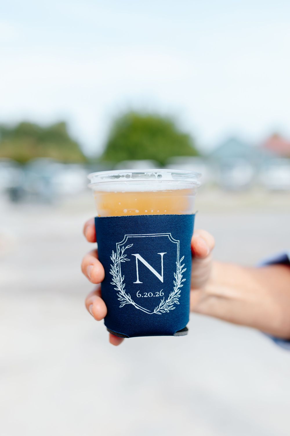 Hand holding a plastic cup in a navy blue koozie monogrammed with letter N and date 6.20.26.