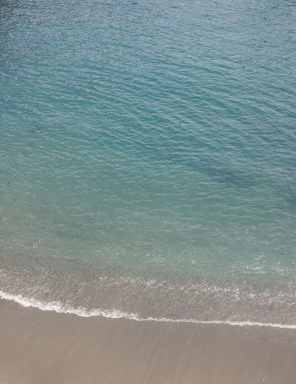 Aerial view of clear turquoise ocean waves gently washing onto a sandy beach shore.
