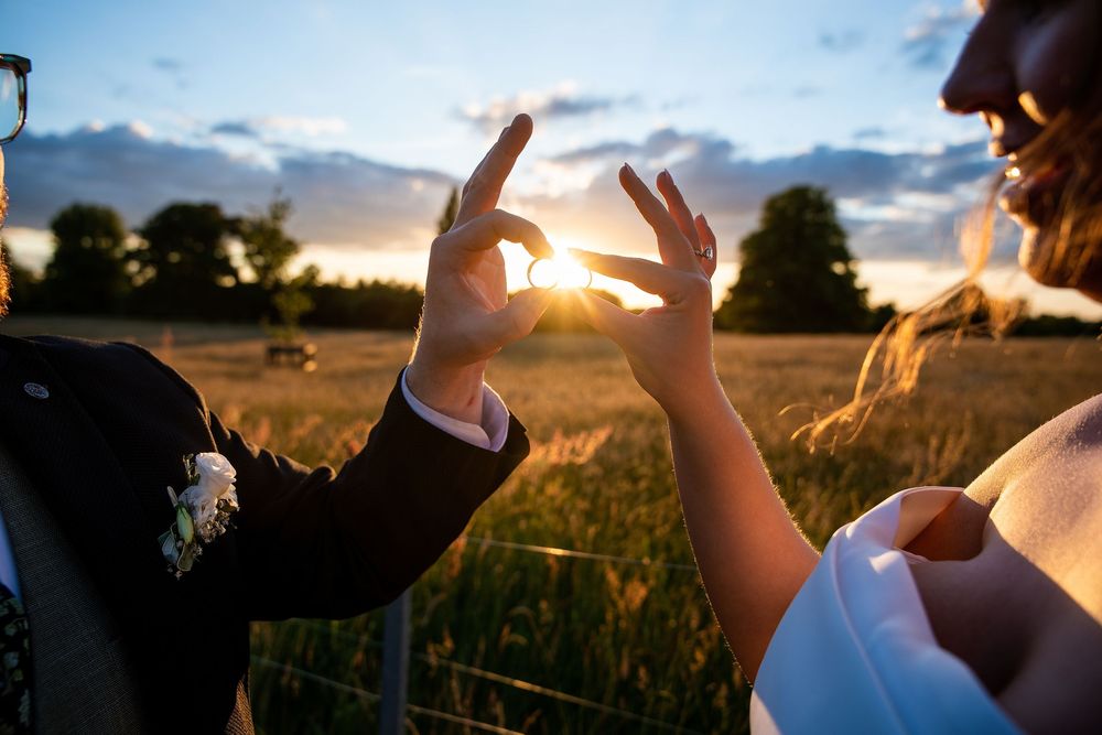 Couple framing the golden sunset through their fingers in a romantic outdoor wedding photo at dusk.