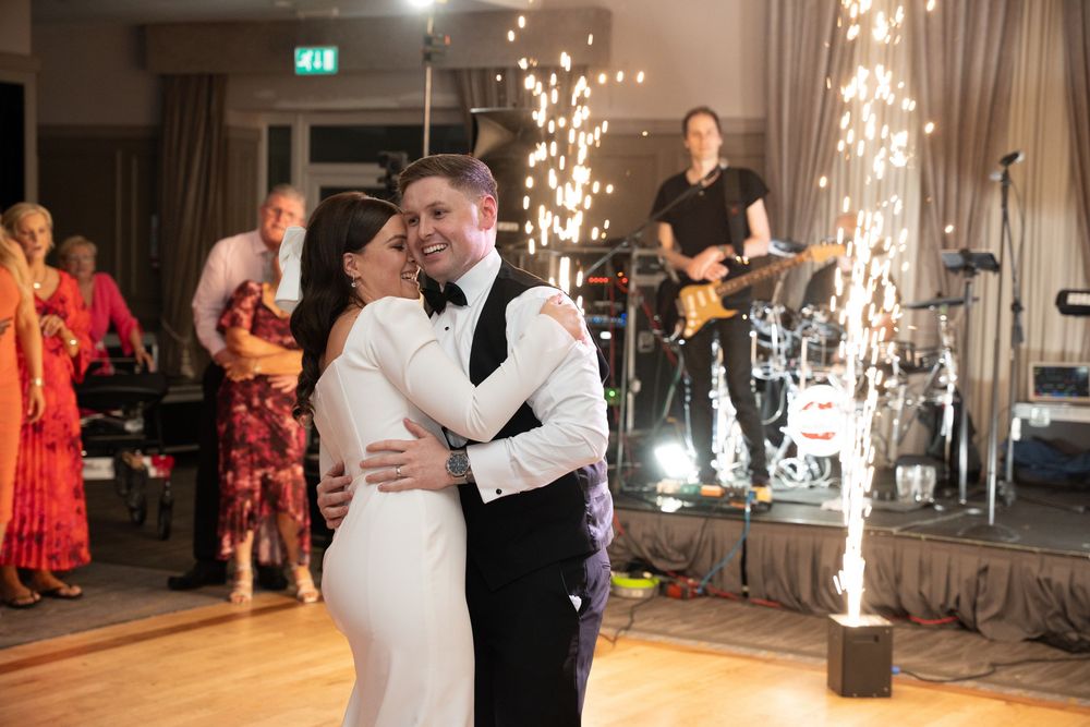 Bride and groom share first dance with sparklers and live band performing at elegant wedding reception.