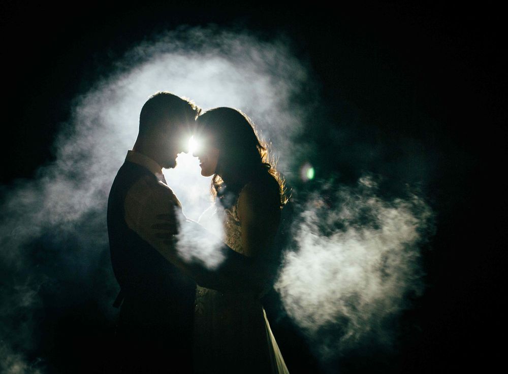 Romantic couple silhouetted against dramatic smoke and light, sharing an intimate moment in the dark.