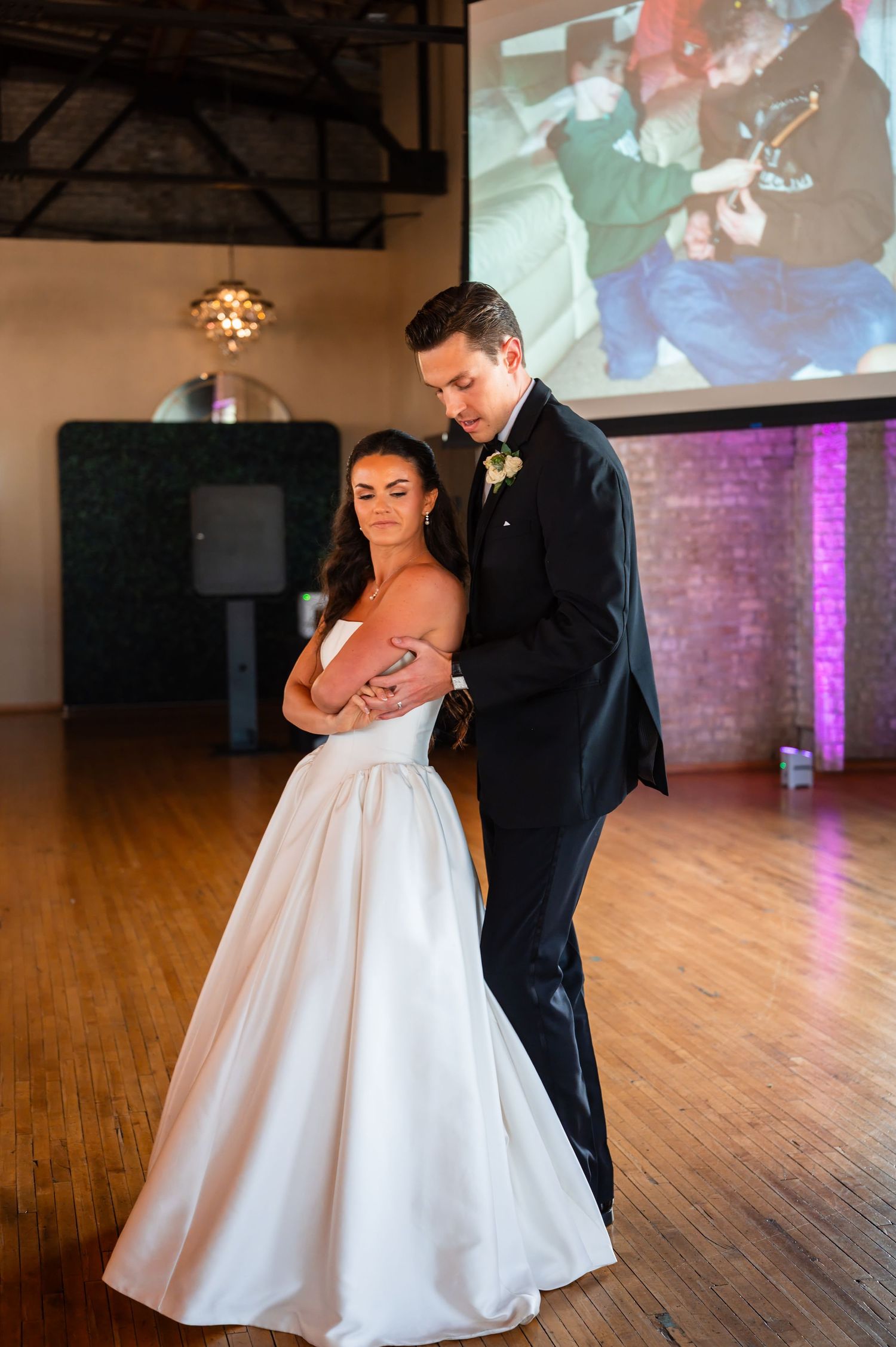 Bride and groom share an intimate first dance at their wedding reception with a projection screen and purple lighting behind them.