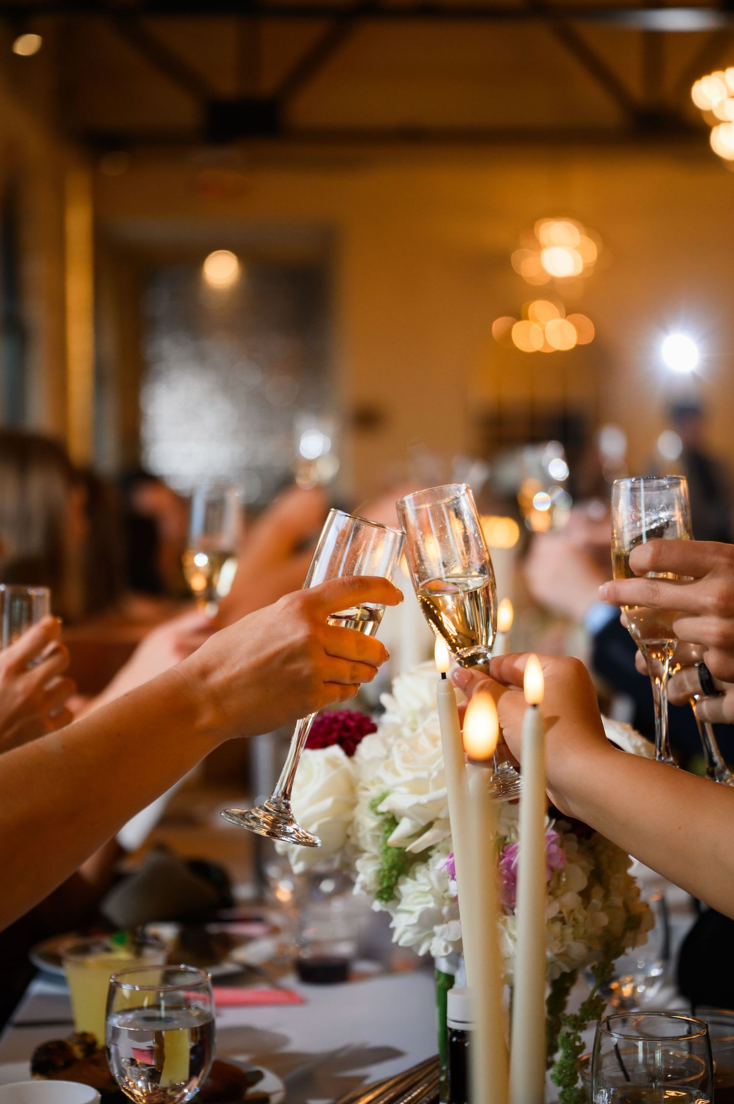Guests raising champagne flutes in a celebratory toast at an elegant candlelit wedding reception dinner.