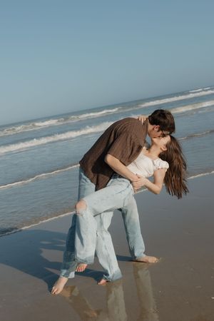 A romantic couple shares an intimate dance pose on a sandy beach with ocean waves in the background.