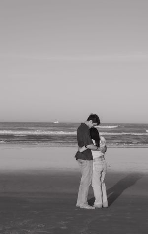 A romantic couple embraces while standing on a misty beach in black and white.