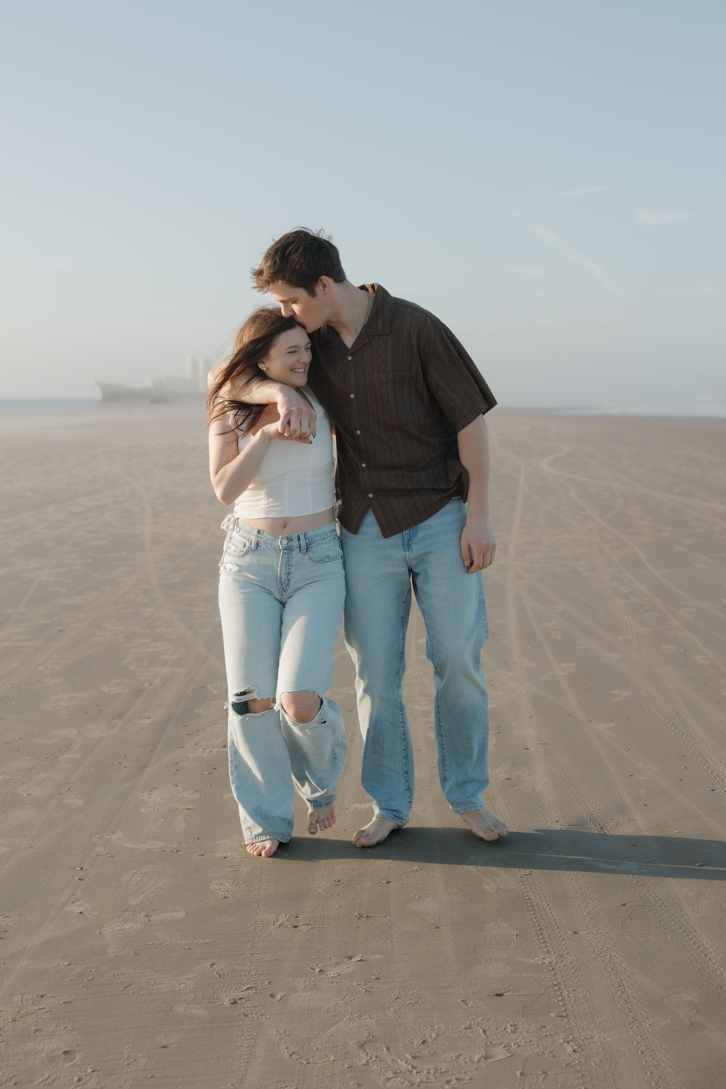 A couple shares an intimate moment together on a sandy beach during sunset.