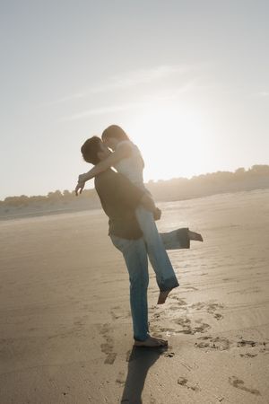 Silhouetted couple embracing on a beach at sunset with bright backlighting creating a romantic atmosphere.