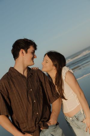 Young couple sharing a joyful moment on the beach during golden hour wearing casual summer outfits.