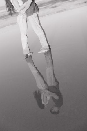 Black and white reflection of two people standing together on wet beach sand.