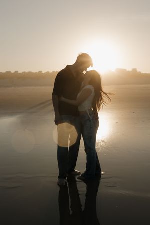 Silhouetted figures embrace on a misty beach at sunset creating a romantic atmospheric scene.