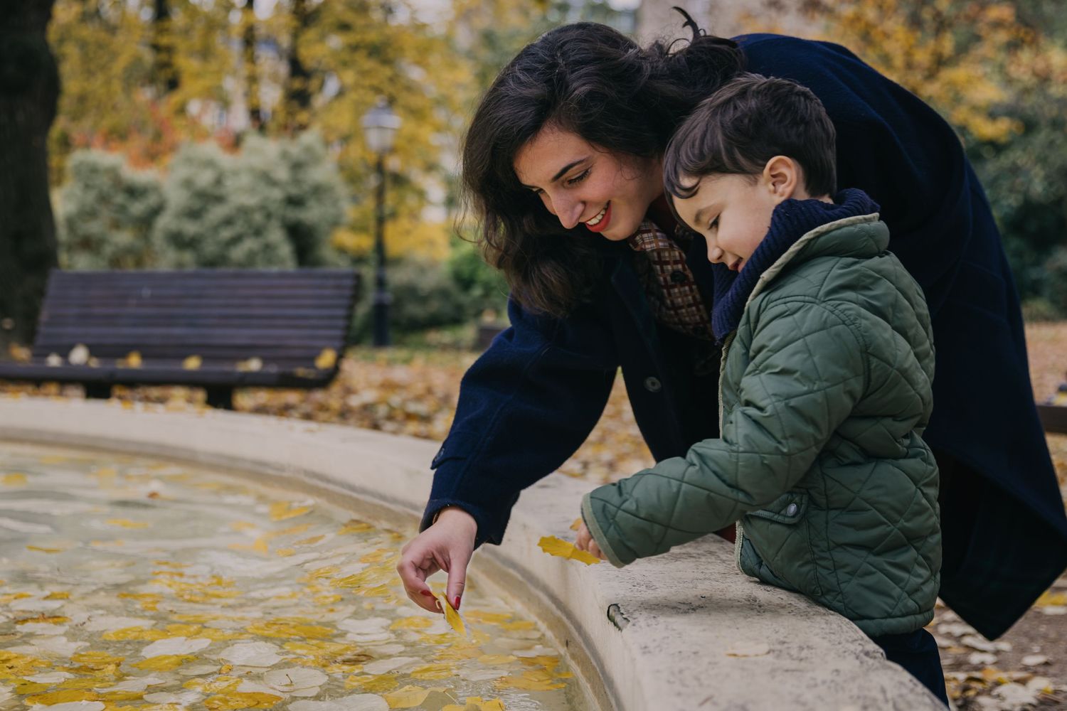 La photographe s'éloigne pour laisser la mère et le fils timide jouer avec les feuilles d'automne sur l'eau de la fontaine à Courbevoie