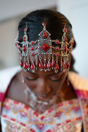 Woman wearing ornate silver and red gemstone crown headpiece with dangling ruby teardrops at a cultural wedding ceremony.