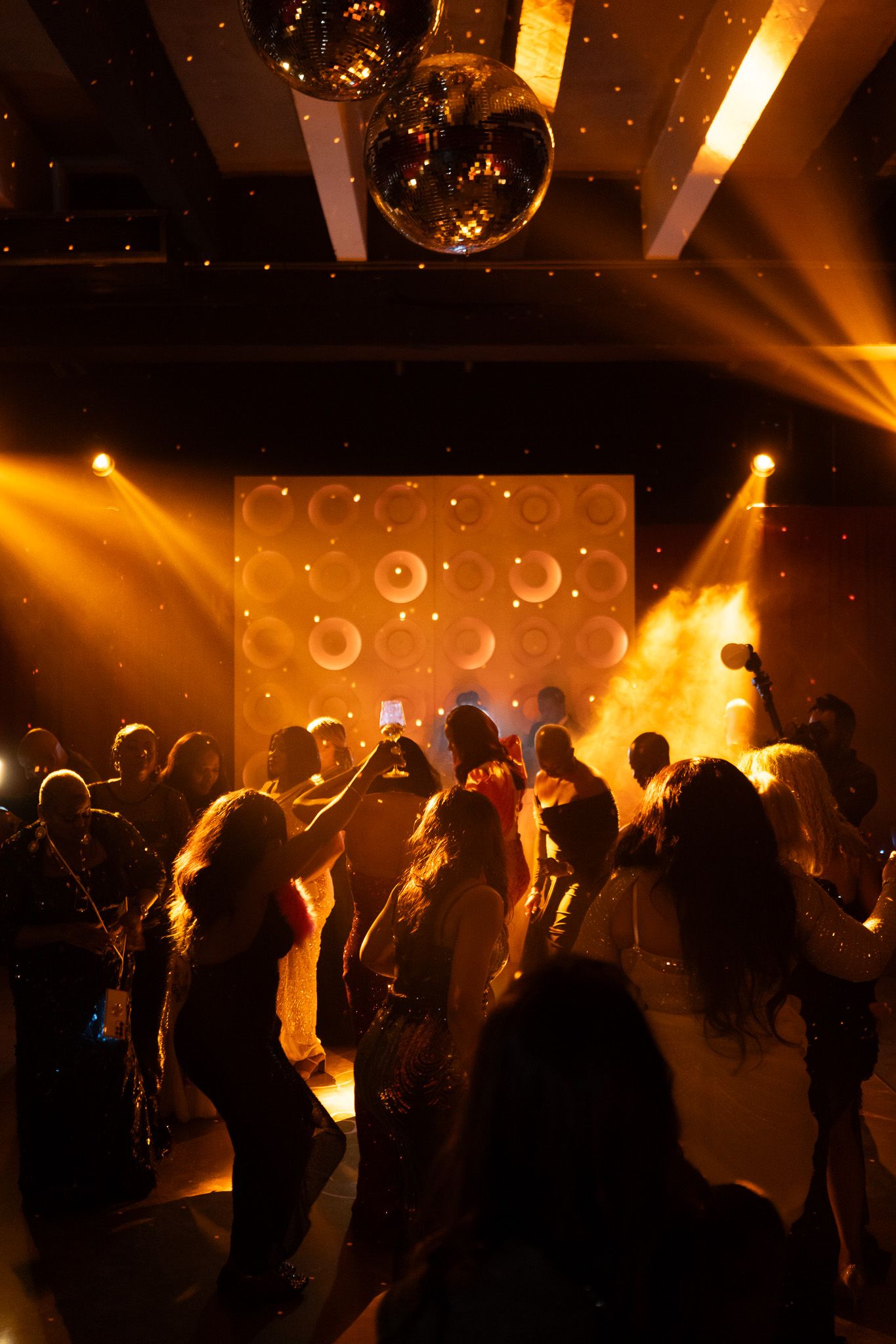 People dancing in a nightclub with golden lighting, disco ball, and circular pattern backdrop.